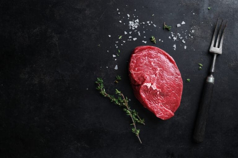 Raw beef portion on a dark surface with thyme, sea salt and a carving fork
