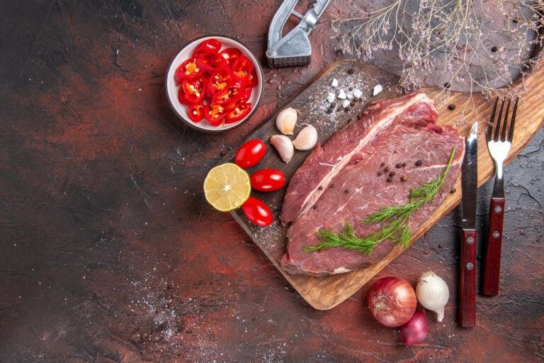 Raw beef cut on a wooden board with garlic, tomatoes, lemon and herbs